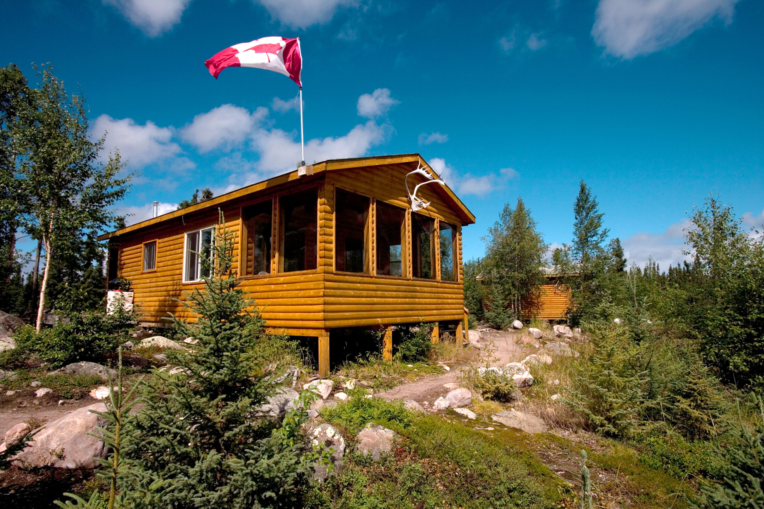 Gangler's Cabin on Maria Lake surround by blue skies and a raised Canadian flag