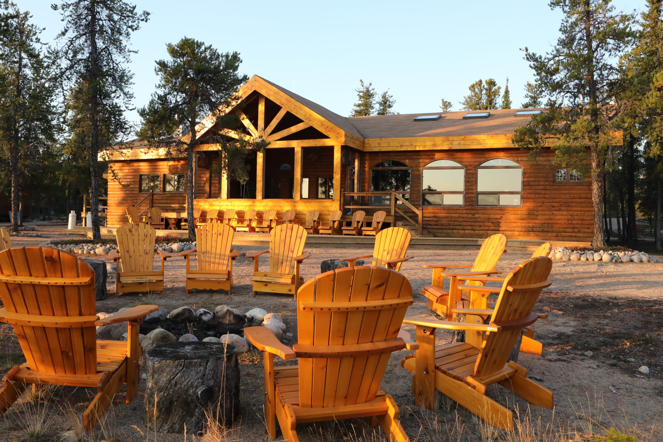 landscape image of a campfire circle with lounging chairs and a main wooden lodge in the background
