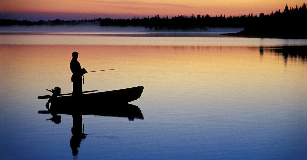 A fisherman in a boat at a luxury fishing destination waits for his catch while the sun is rising in the morning.