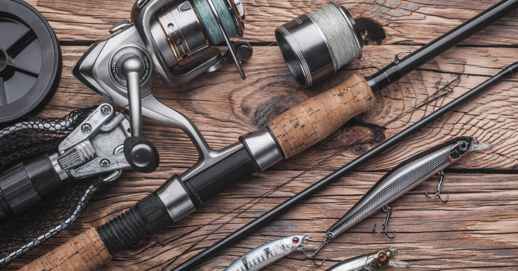 A worn, brown wooden table that has an assortment of rods, reels, and other high-quality fishing gear lying across it.