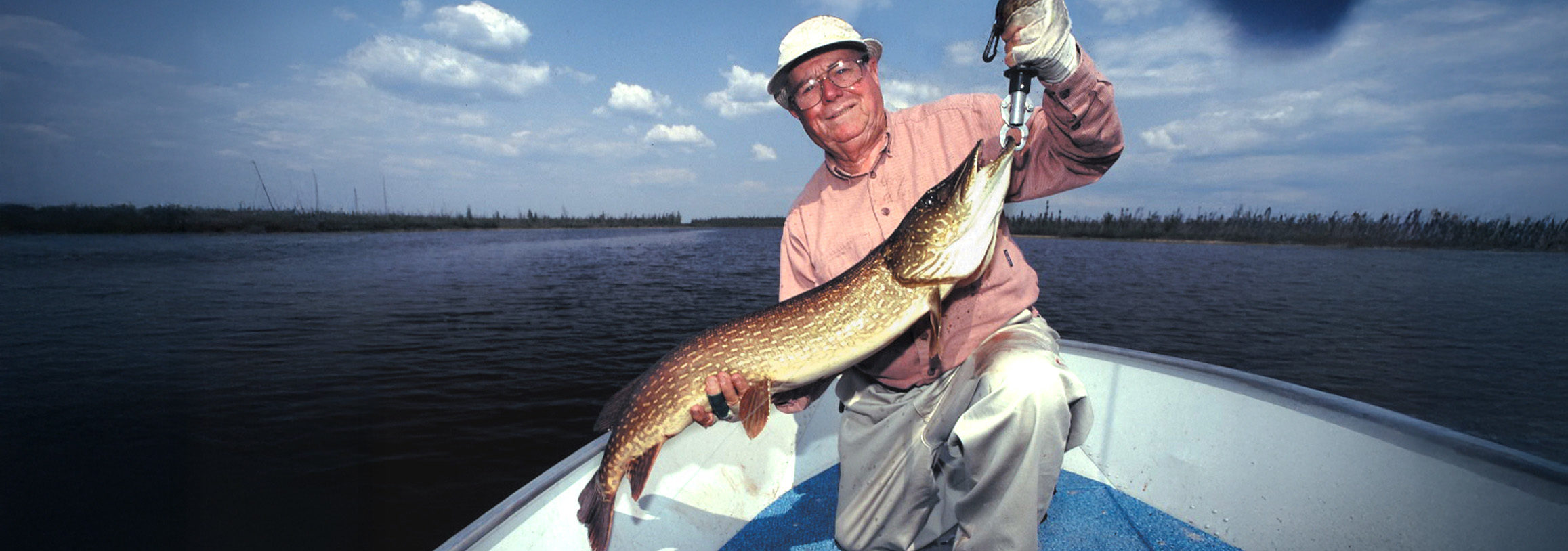 Image of Lefty Kreh holding up a large pike while in a boat.